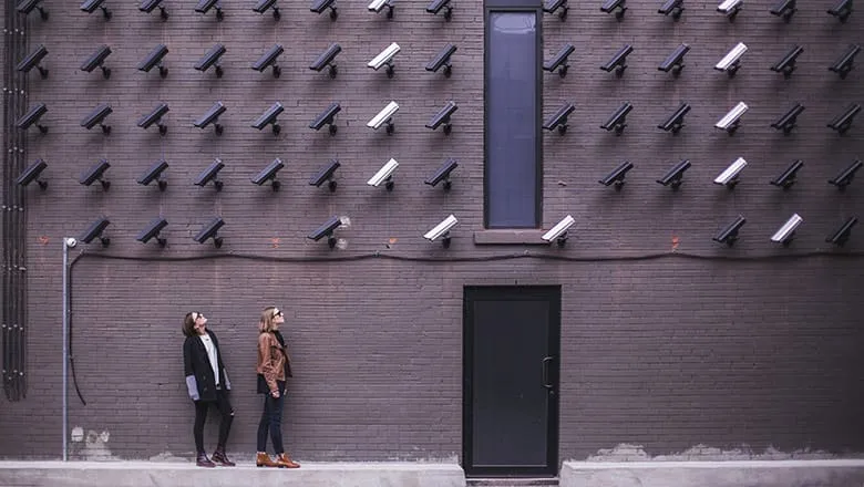 Two people standing under a brick wall covered with surveillance cameras